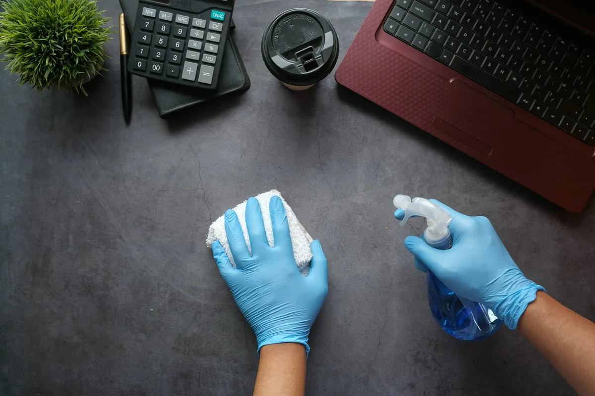 Hände in blauen Handschuhen wischen einen Schreibtisch ab
